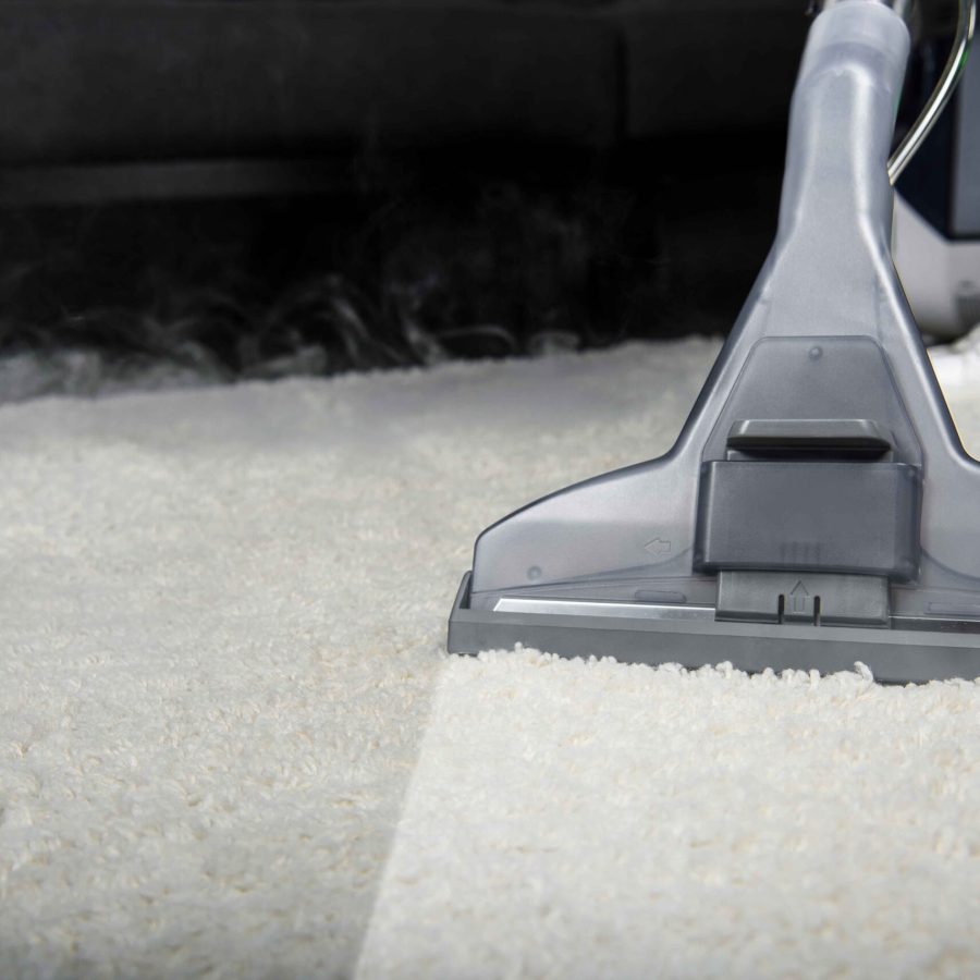 close-up view of person cleaning white carpet with professional vacuum cleaner