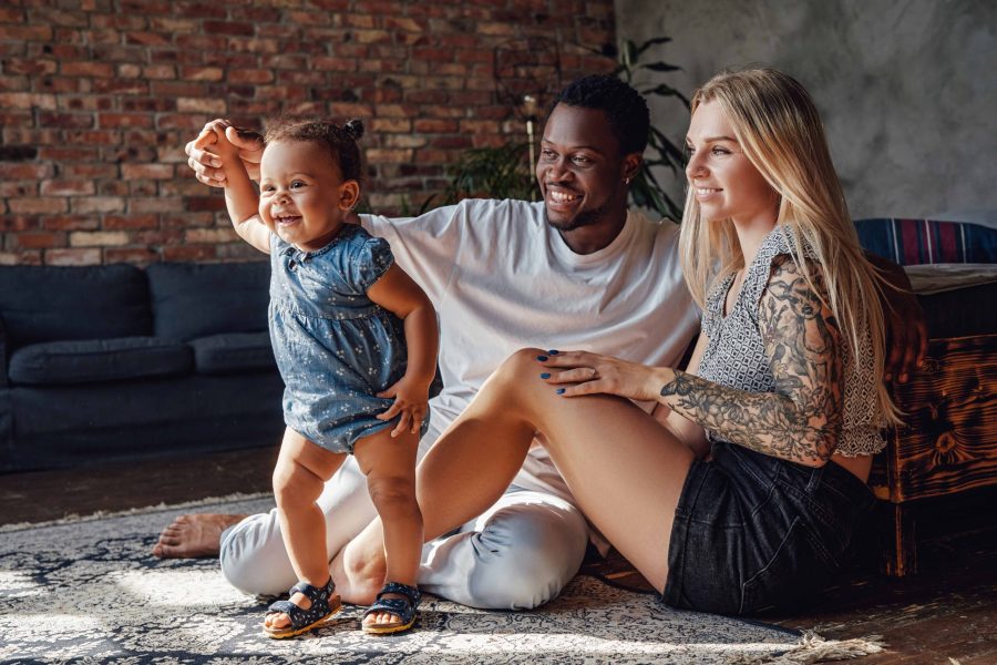 Shot of caring multiethnic couple and their daughter inside modern apartment in sunny day.